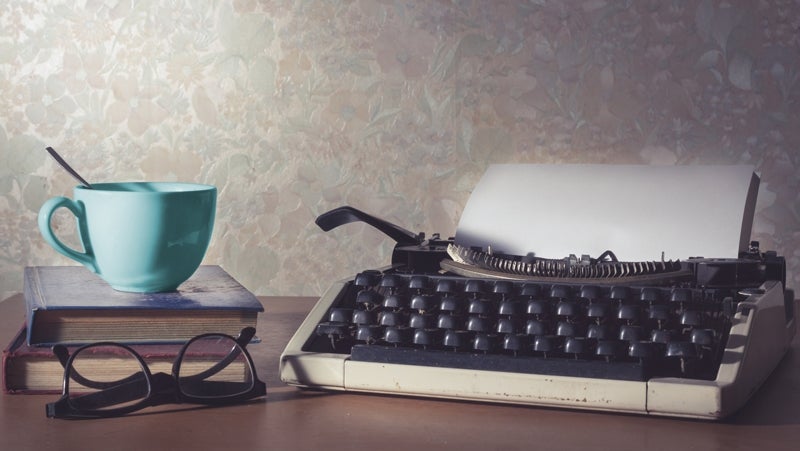 Photo of typewriter with book and cup.