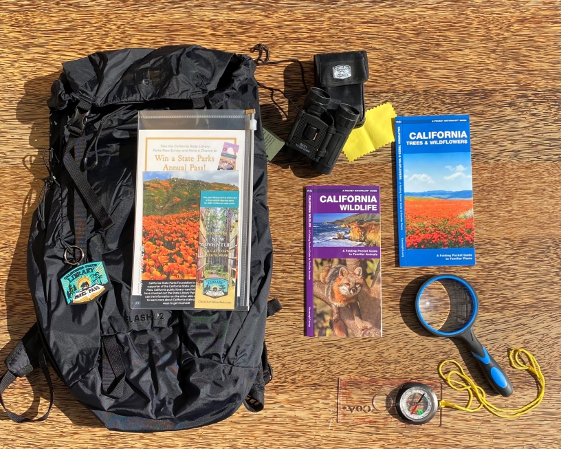 Backpack next to maps, magnifying glass, compass, and other outdoor items