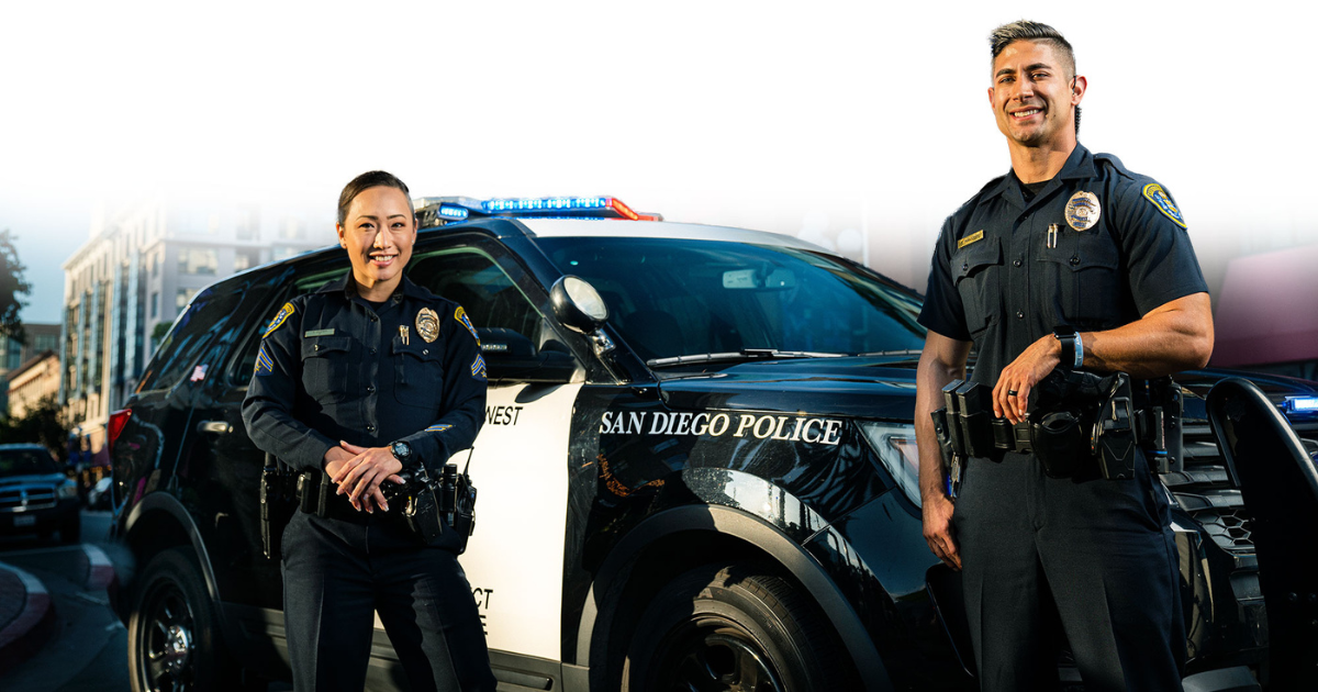 two police officers standing next to a cop car smiling
