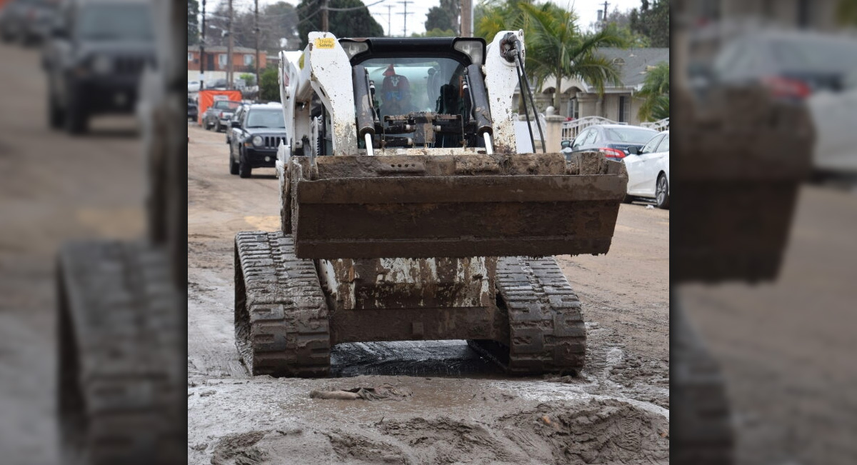 City worker in a bulldozer cleaning up mud on a street