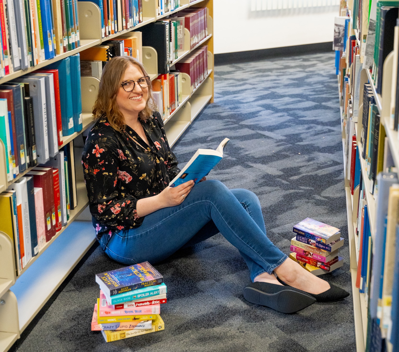 Librarian holding a book open while sitting down next to piles of books