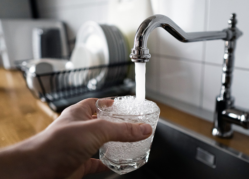 Person holding a glass being filled with water from a faucet
