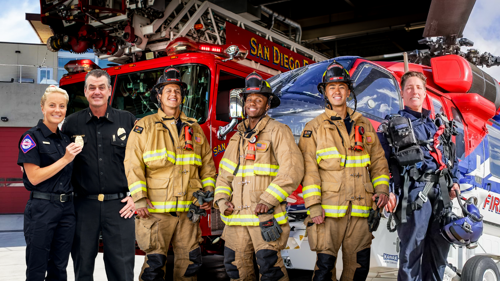 Five San Diego Fire Fighters standing in their gear, in front of a fire station, fire truck and helicopter. 