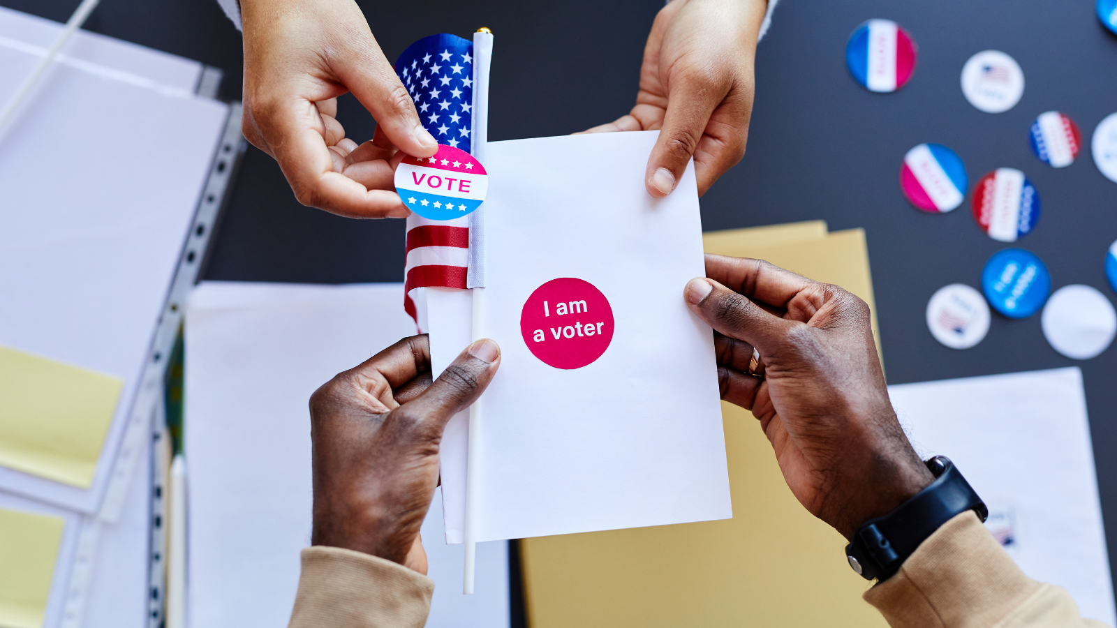 once person handing off a paper, sticker and USA flag showing they are registered to vote