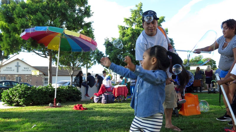 A family playing with bubbles on the lawn in front of the Logan Heights Library