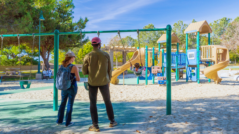 A man and woman pushing a child on a swing at the Torrey Hills Park playground