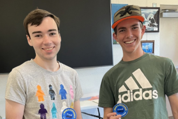 Two young men in a community room smile while holding stickers