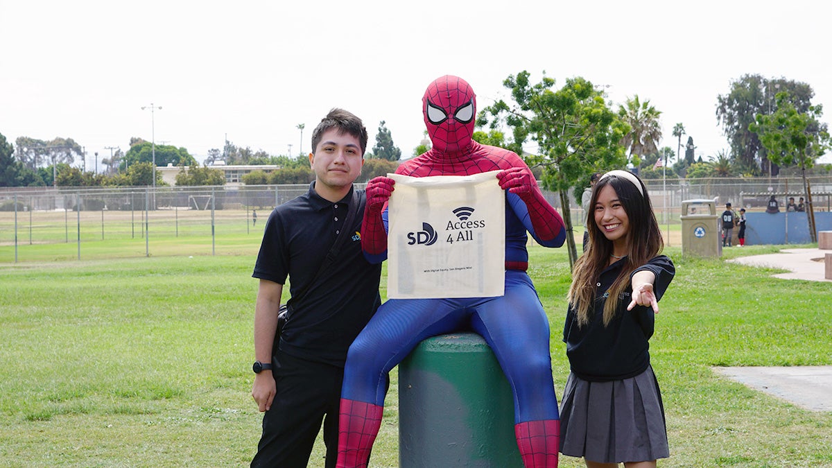 Digital Navigator Program volunteers posing for a picture with a person dressed as Spiderman at a park