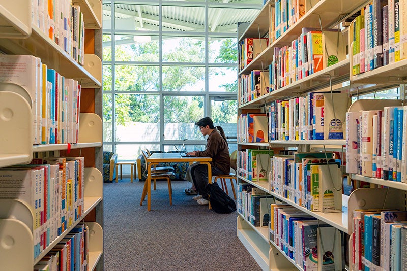 A person sitting at a table at the end of two library book shelves at Rancho Peñasquitos Library