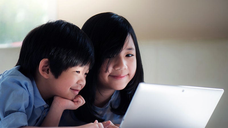 Two Asian children looking at a laptop monitor