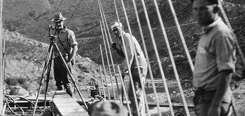 Black and white photo of a videographer filming the construction of a bridge