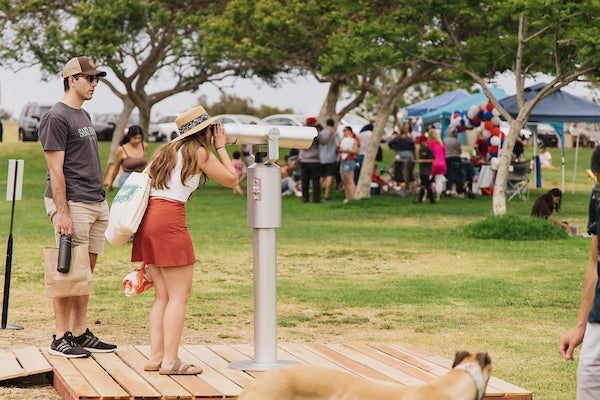 A park visitor looking into binoculars that display video vignettes of everyday workers who make the city of San Diego run