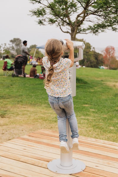A park visitor looking into binoculars that display video vignettes of everyday workers who make the city of San Diego run