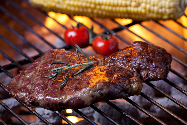 Steak, tomatoes, and corn on a grill