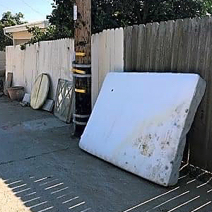 Old mattress leaning against a fence along a public sidewalk