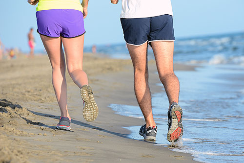 Close up legs of man and woman running on the beach