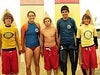 A picture of five kids standing in front of surfboards