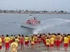 A lifeguard on a motor boat spraying water towards children on the beach