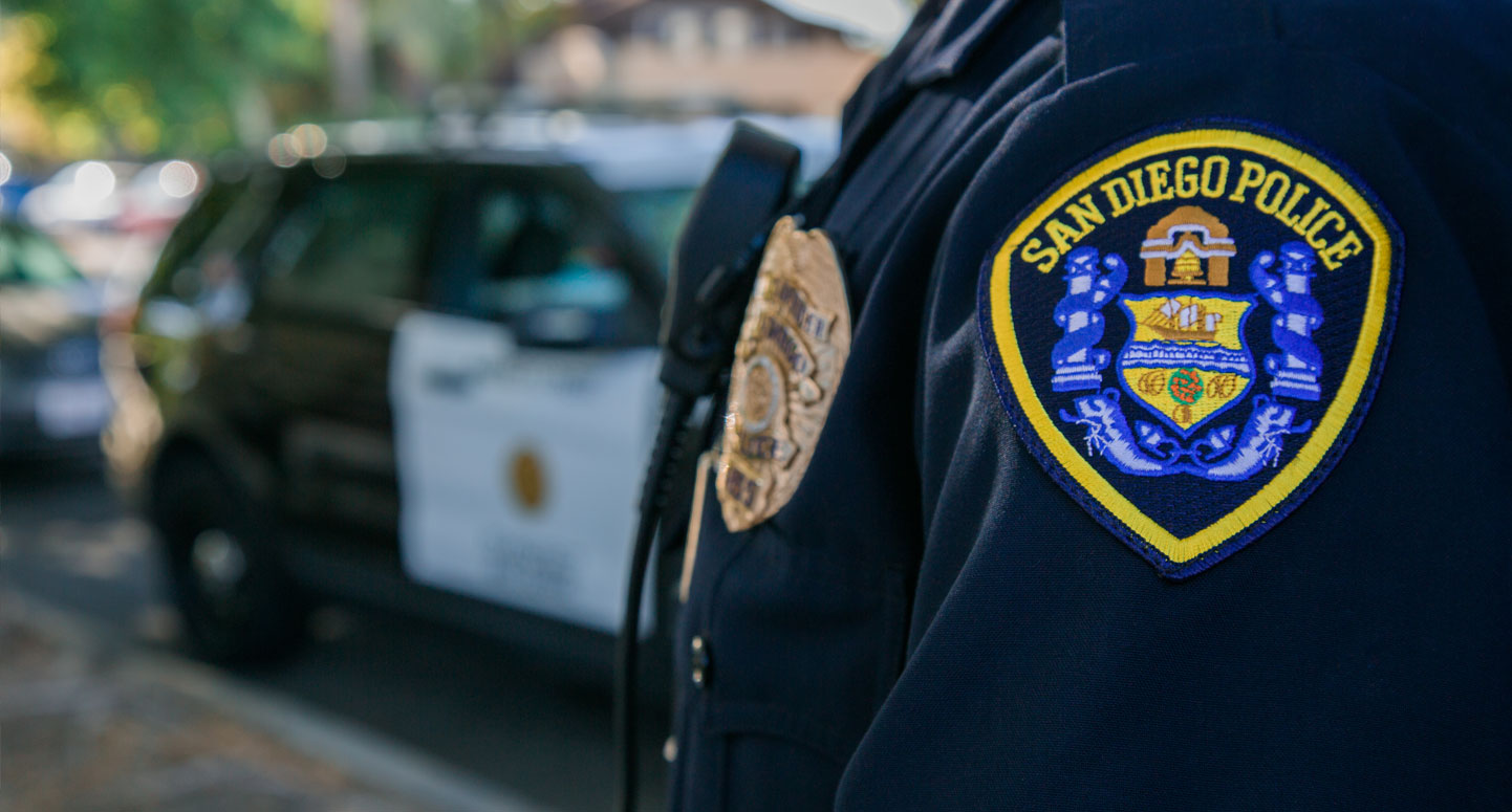 San Diego Police badge on side of uniform with a police car in the background