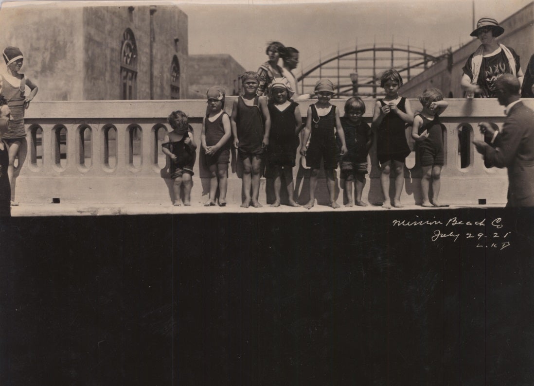 Eight young children at Mission Beach standing at seawall circa 1921