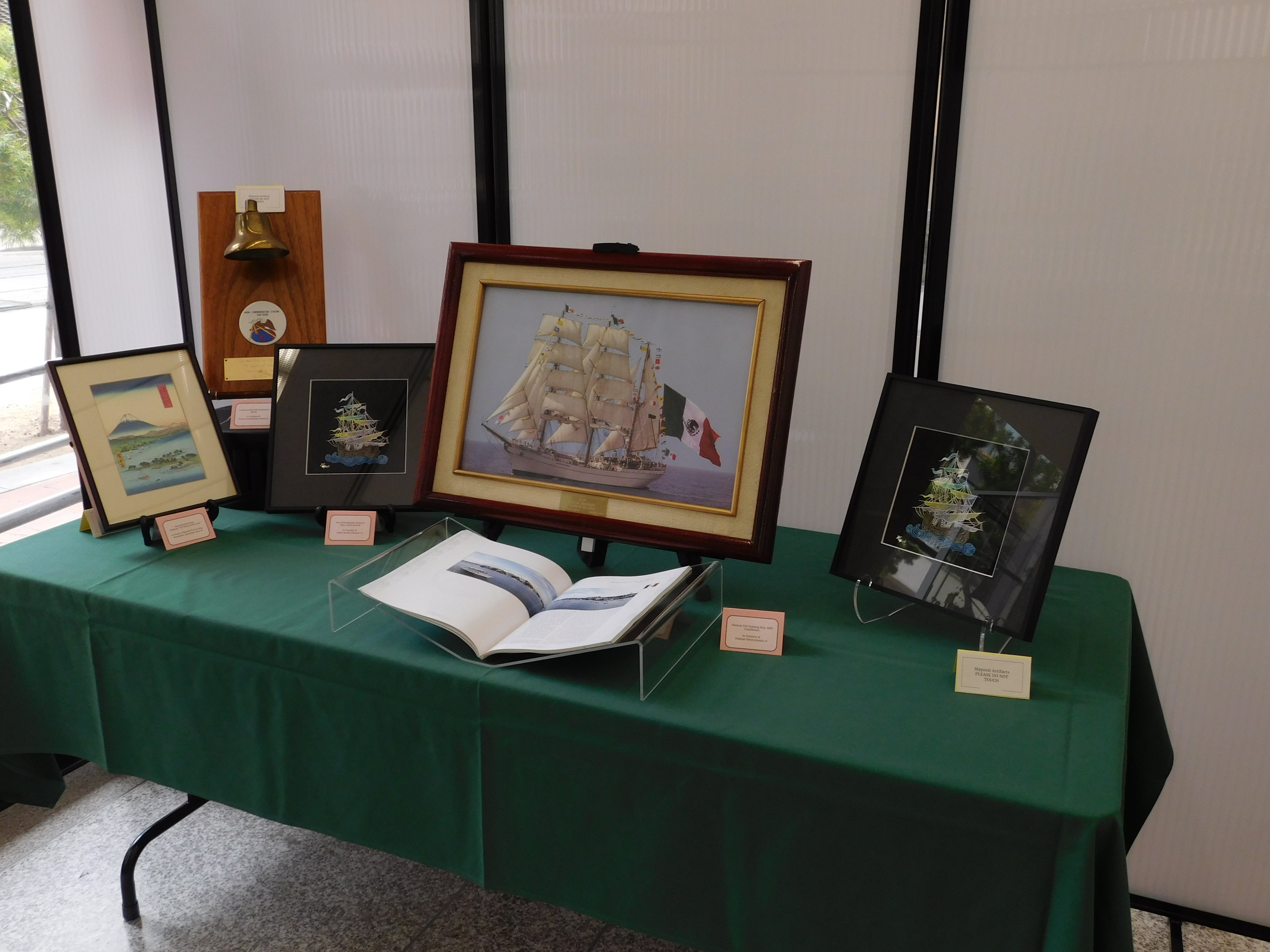 Image of back right table includes bell&#44; cloisonne ship decorations&#44; Japanese block print of ships&#44; and Mexican tallship photo.