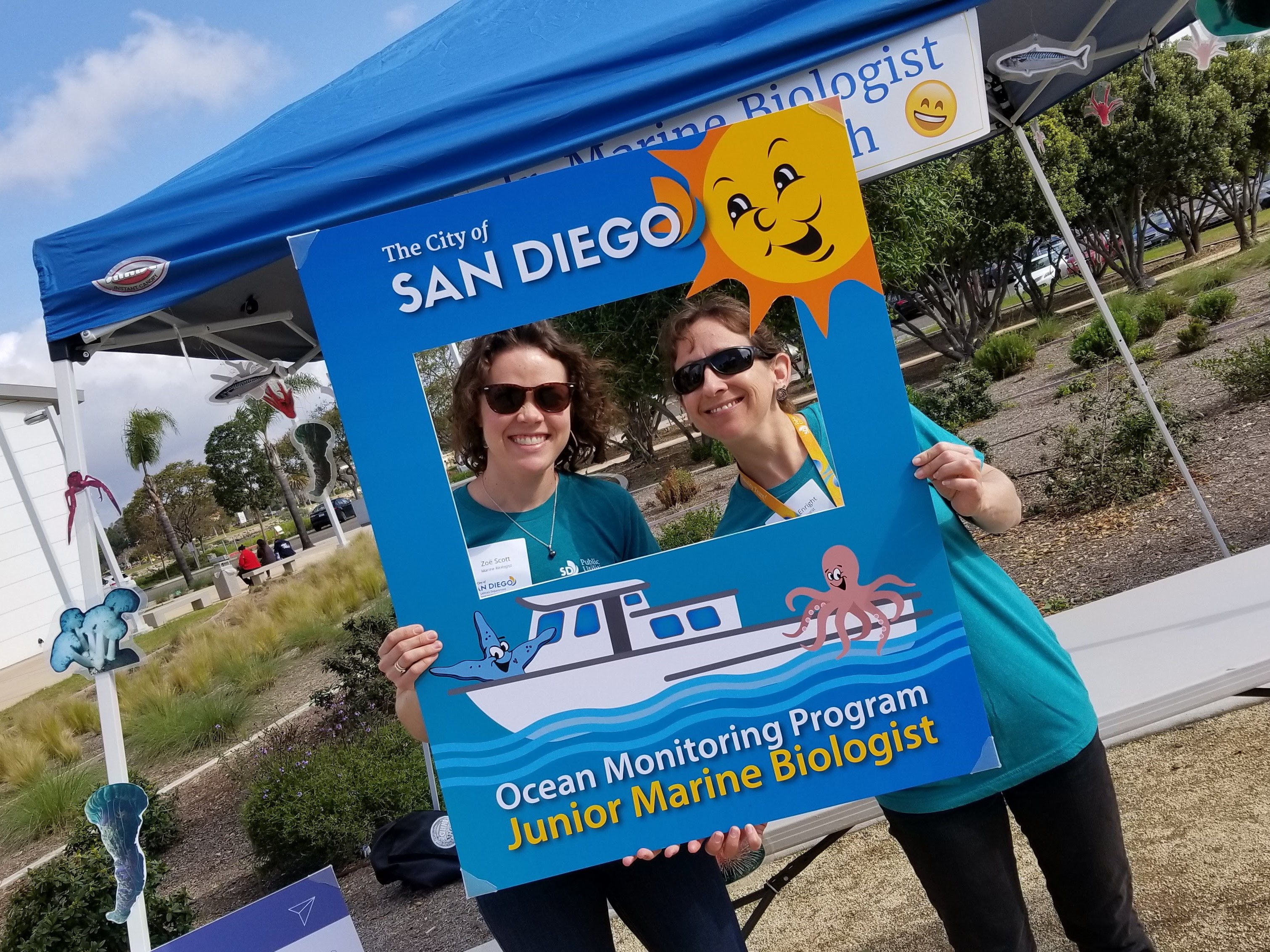 Two marine biologists pose with a social media frame at the Ocean Monitoring Program's Open House event.