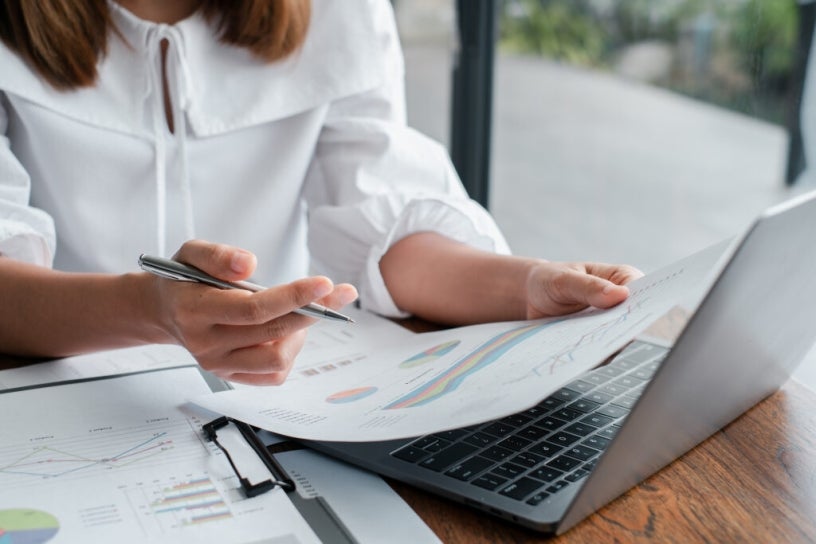 A woman with a laptop reviewing a document with charts
