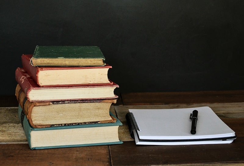 Stack of books next to a notepad and pen