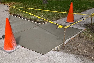 New sidewalk concrete surrounded by caution tape and red cones