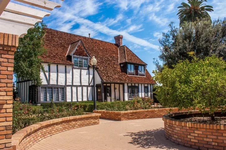 A two story house built in 1928 in the English Tudor style, white plaster and wooden frames with a hip-gabled roof clad in cedar shingles. 