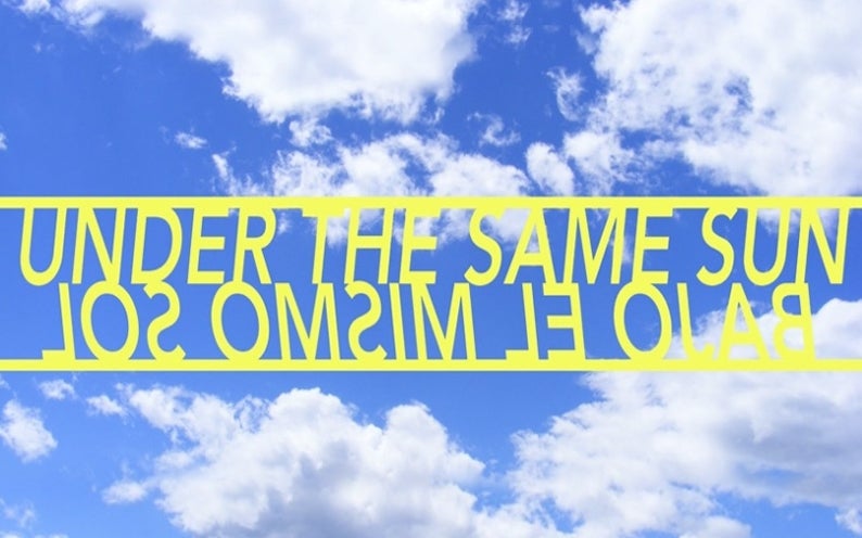 yellow lcut-out letter Sign that says under the same sun and bajo el mismo sol  viewed from below so sky can be seen through it