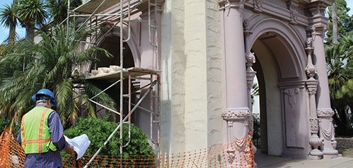 A building inspector in personal protective equipment reviews plans in front of a construction site at Balboa Park. 