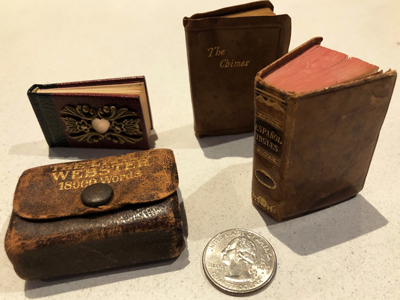 Image of four miniature books next to a quarter for size comparison