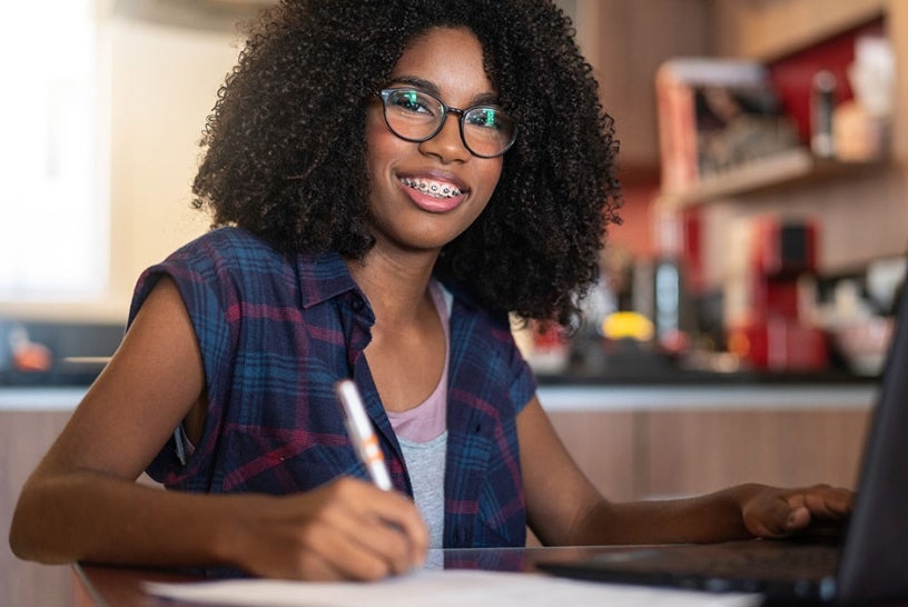 Young girl working on a laptop with notebook and pen.