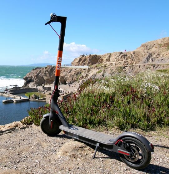 A shared mobility device from Spin parked on a mountain overlooking the ocean.