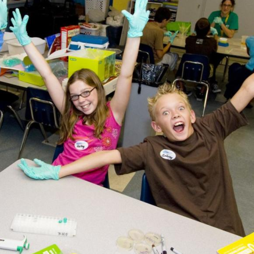 Two excited kids with gloves at a table.