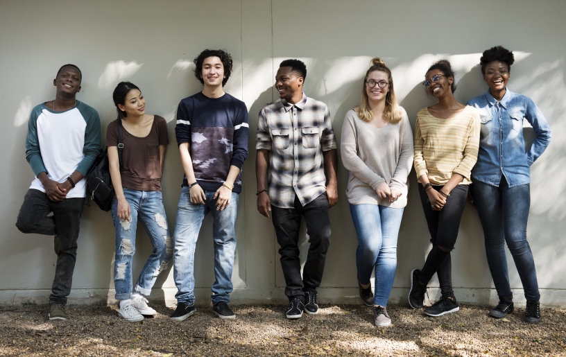 Seven teens standing against a wall smiling