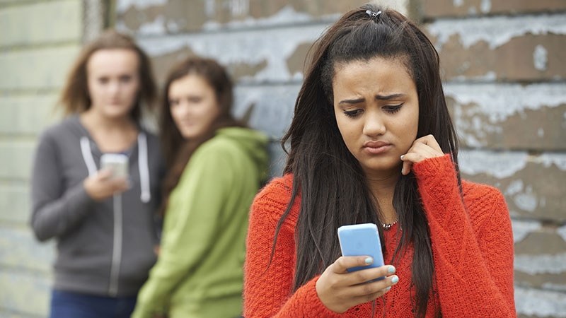 Teenage girl with smartphone being cyberbullied by girls behind her