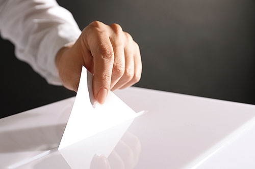Woman putting her vote into ballot box on black background