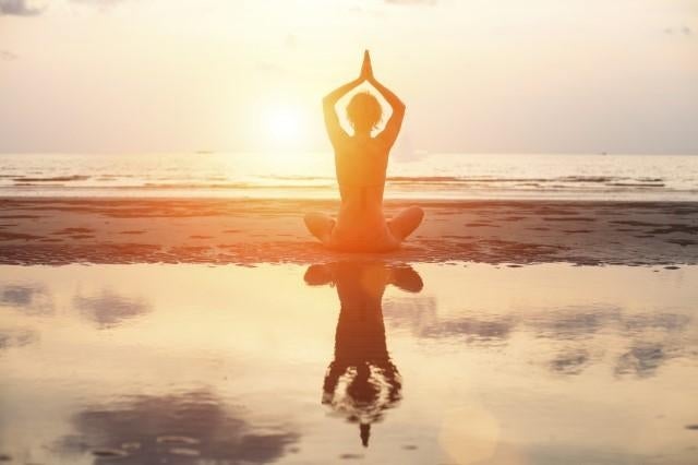 Silhouette of a person in a yoga pose sitting on the beach at sunset