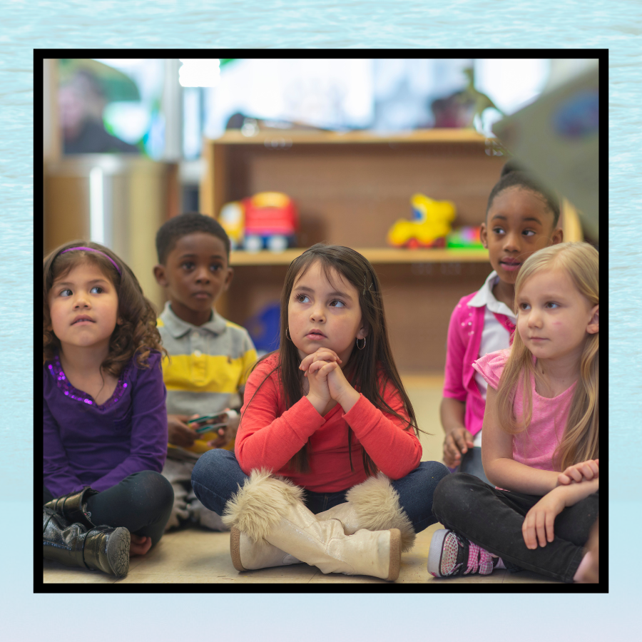 A group of children listen attentively to storytime. The photograph is framed in a pale blue background.