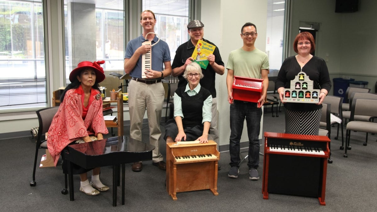 Image of six musicians at UC San Diego Library, standing and sitting, with toy pianos and book