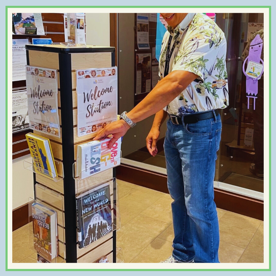 A patron is taking a book from a Welcome Station at a SDPL branch. 