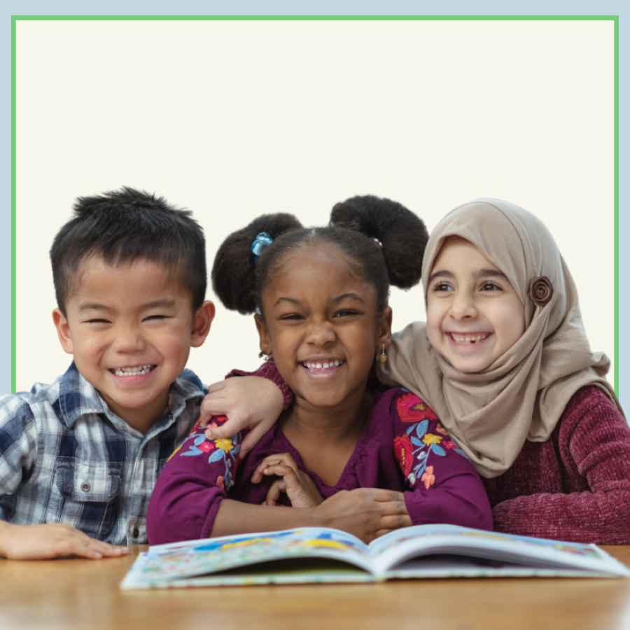A group of three children smile and group around a book.