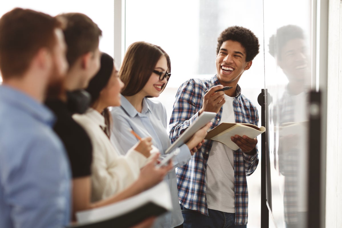 Group of five young adults standing and collaborating in front of whiteboard