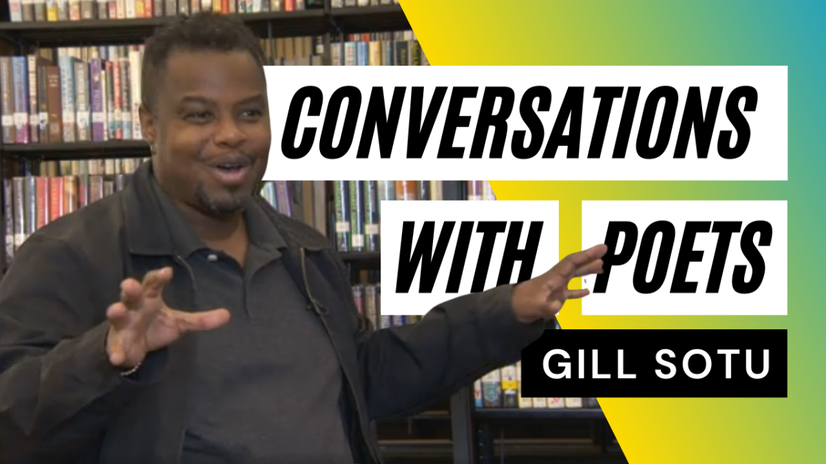 A Black man gestures and smiles in front of book shelving at Central Library.