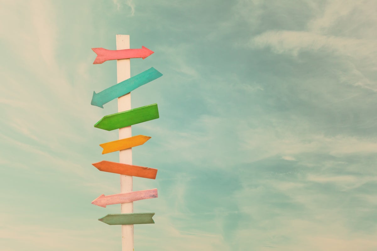 Arrows of various colors pointing different directions on a signpost against a blue and cloudy sky.
