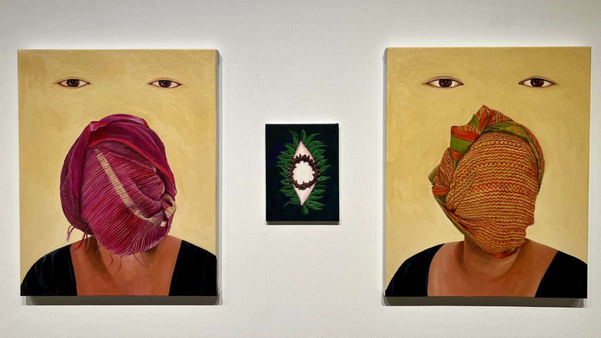 Closeup of an embroidered tunic constructed with multiple pockets by Kirstyn Hom. In the background is a long thin object titled “Amulet for Returning Home” by Shirin Towfiq.