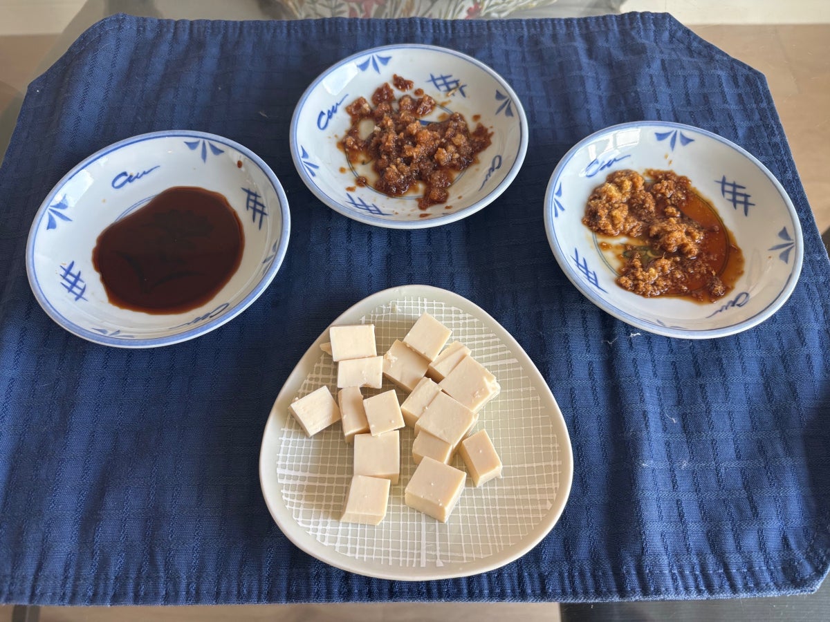 A plate of soft tofu cut into cubes, surrounded by 3 small blue saucers with dipping sauces.  