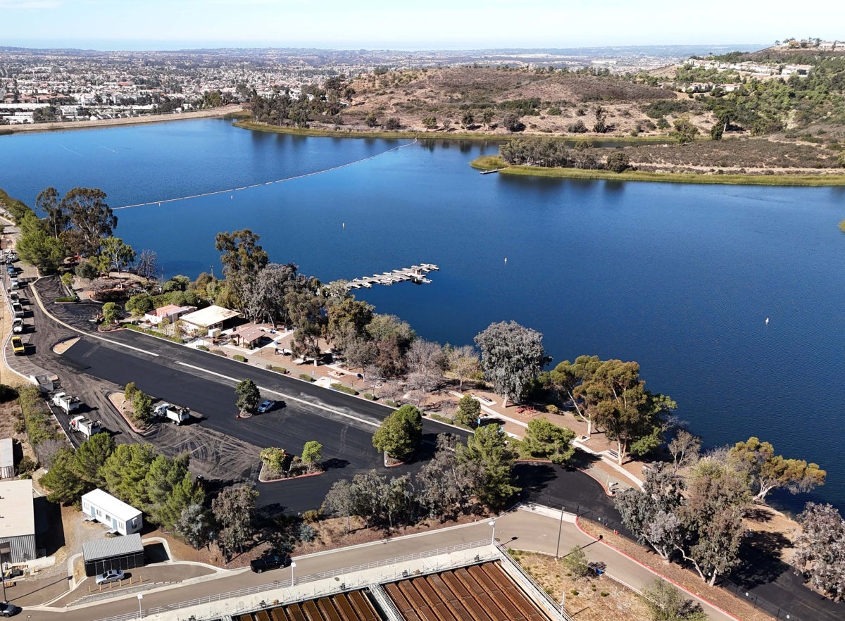 Parking lot paving next to a large blue reservoir surrounded by trees and greenery